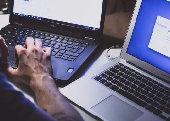 A man typing on two laptop computers